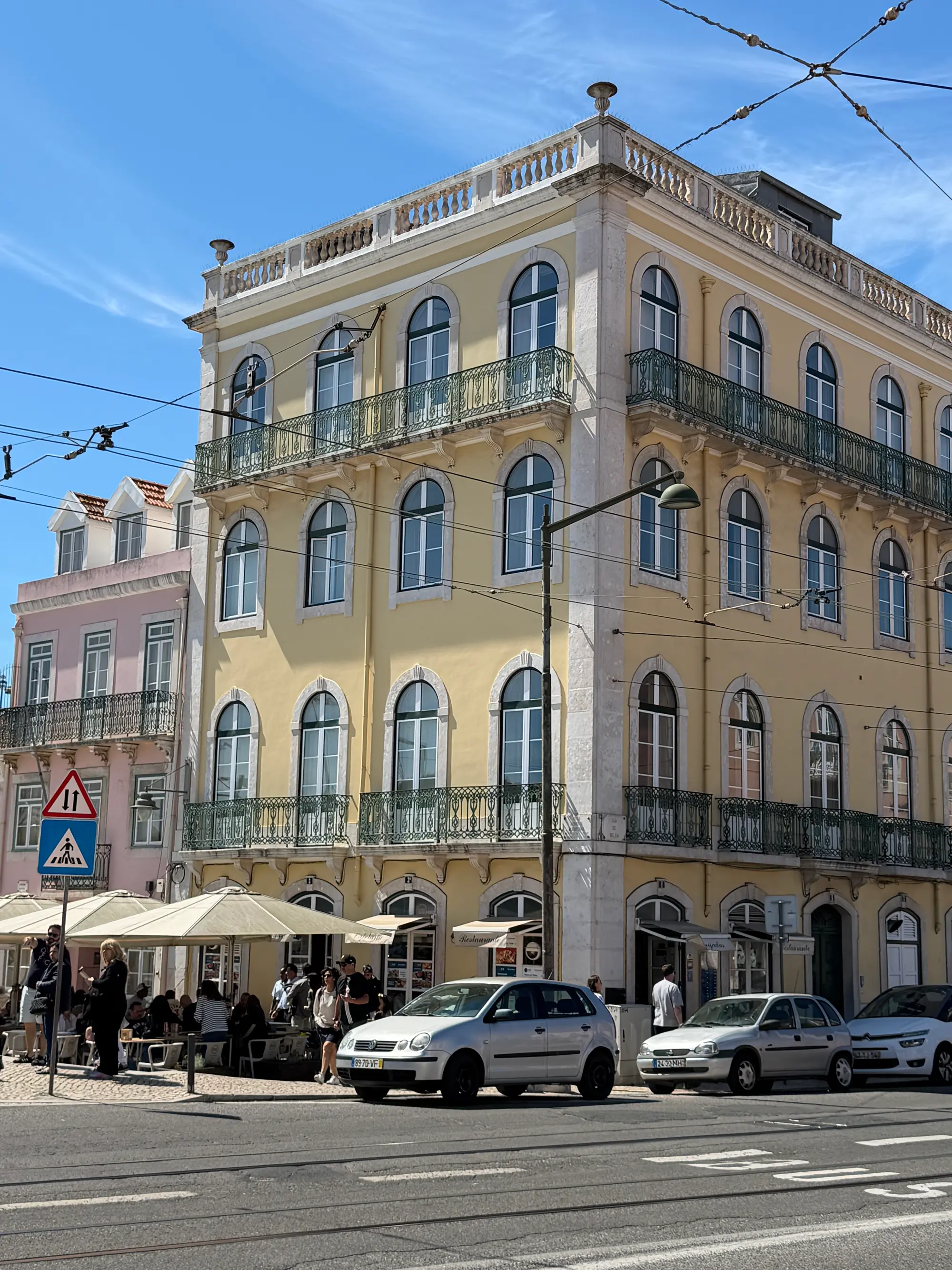Prédio amarelo com janelas em arco e mesas de café ao ar livre numa esquina em Belém, Lisboa.