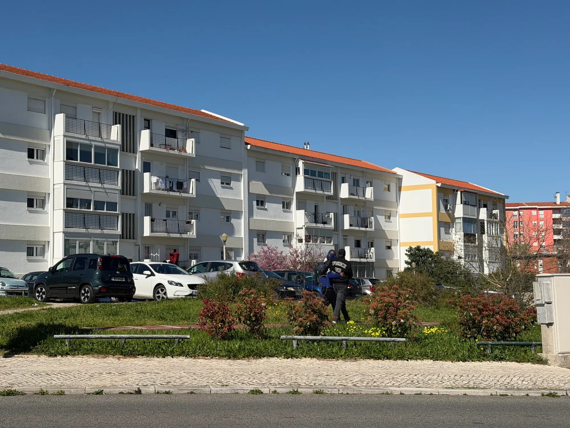 Olivais Lisboa: prédios residenciais com carros estacionados, área verde e pedestres caminhando pela rua.