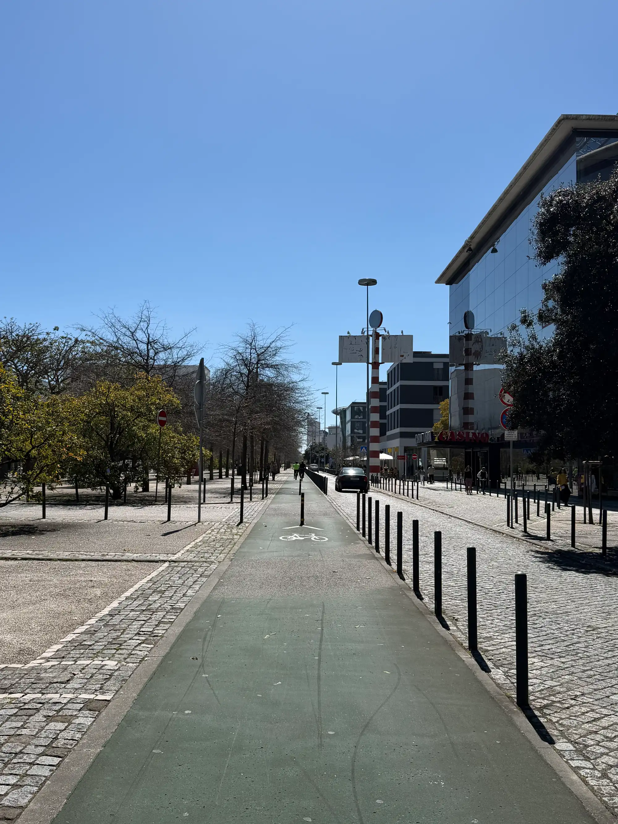 Ciclovia ao longo de uma rua moderna no Parque das Nações, em Lisboa, com edifícios contemporâneos, árvores e céu azul límpido.